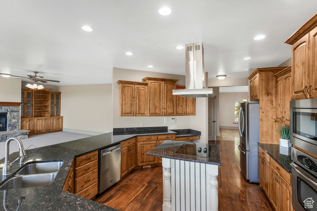 Kitchen with island exhaust hood, appliances with stainless steel finishes, a sink, a ceiling fan, and dark stone countertops