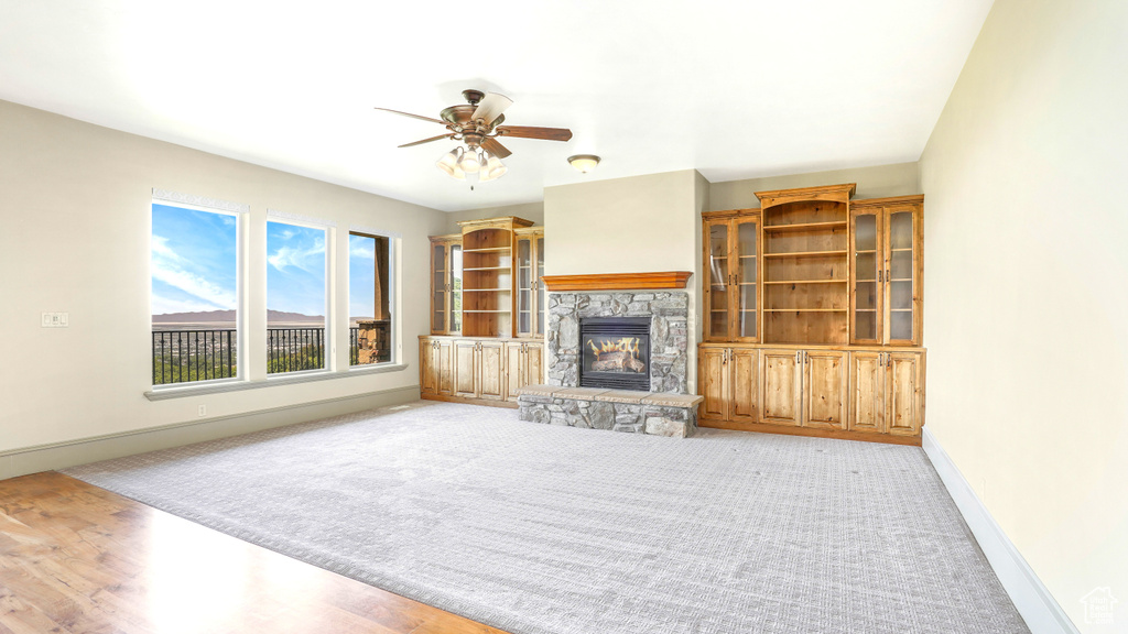 Unfurnished living room featuring a ceiling fan, baseboards, a stone fireplace, light colored carpet, and light wood-style floors