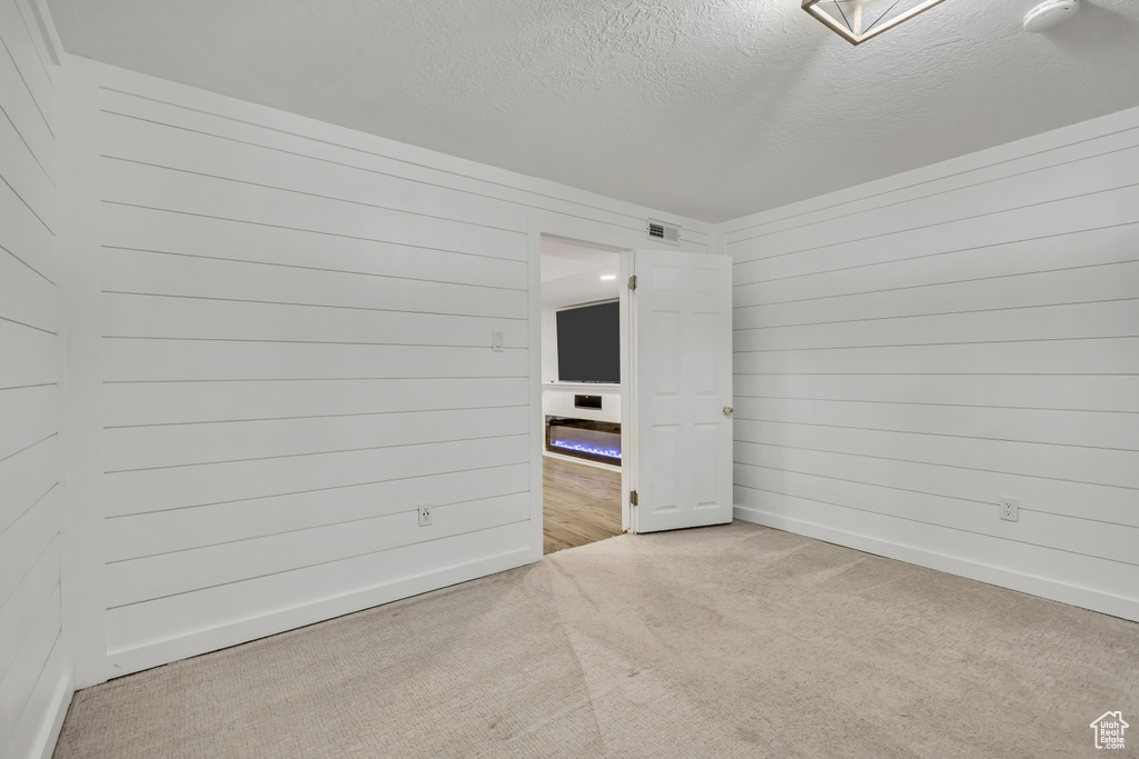 Unfurnished room featuring carpet flooring, a textured ceiling, wood walls, and baseboards