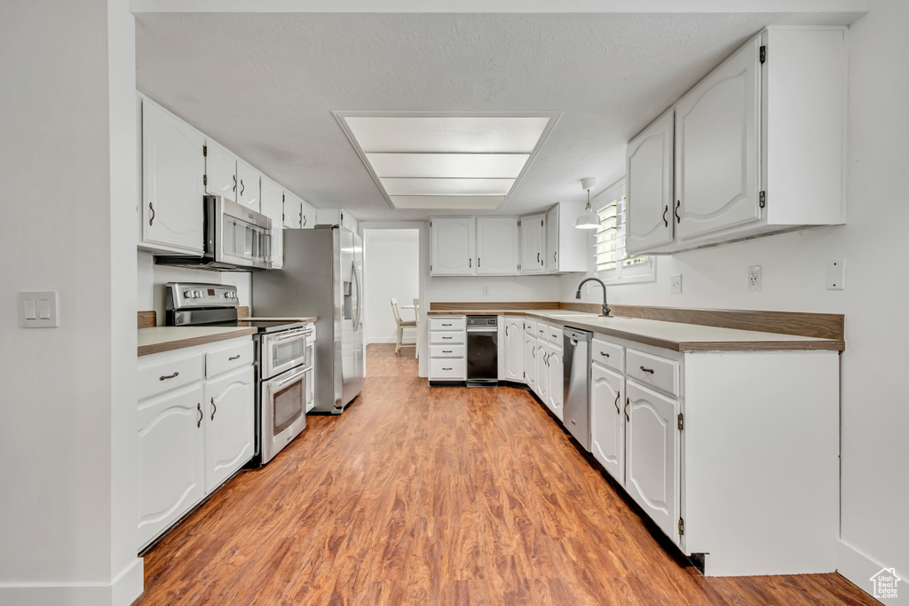 Kitchen featuring stainless steel appliances, light wood-style flooring, a sink, white cabinetry, and light countertops