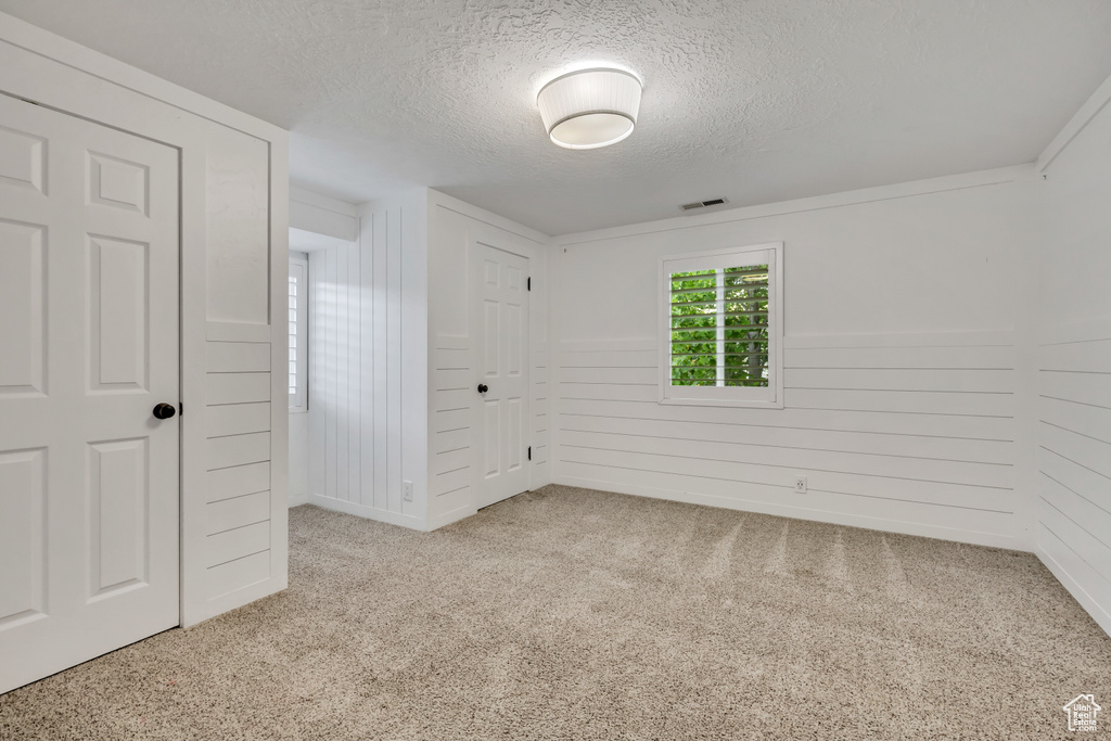 Unfurnished bedroom featuring a textured ceiling, carpet flooring, a closet, and wooden walls