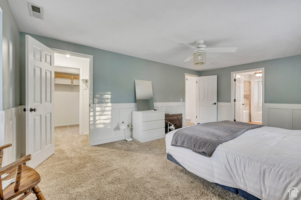 Carpeted bedroom with a spacious closet, wainscoting, a closet, a ceiling fan, and ensuite bath