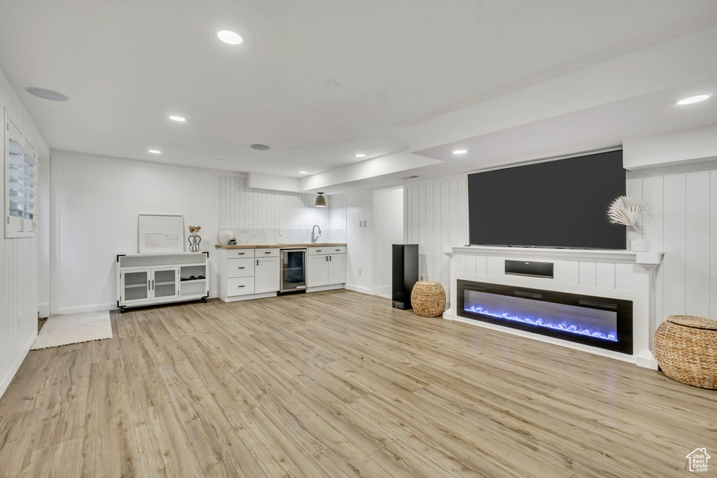 Unfurnished living room featuring wine cooler, light wood-style floors, a sink, a glass covered fireplace, and recessed lighting