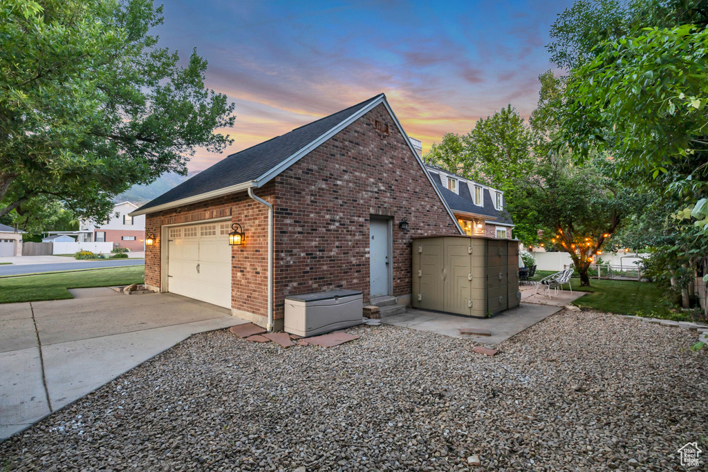 View of side of home featuring brick siding, an attached garage, concrete driveway, and roof with shingles