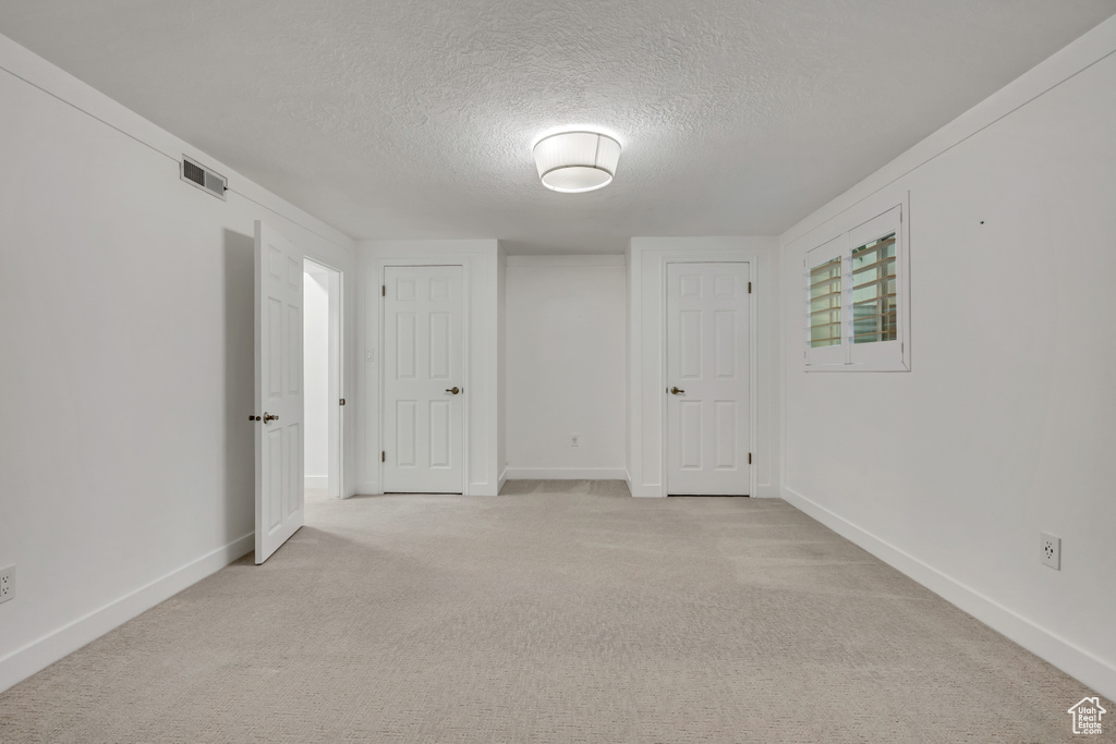 Empty room featuring a textured ceiling, light colored carpet, and baseboards