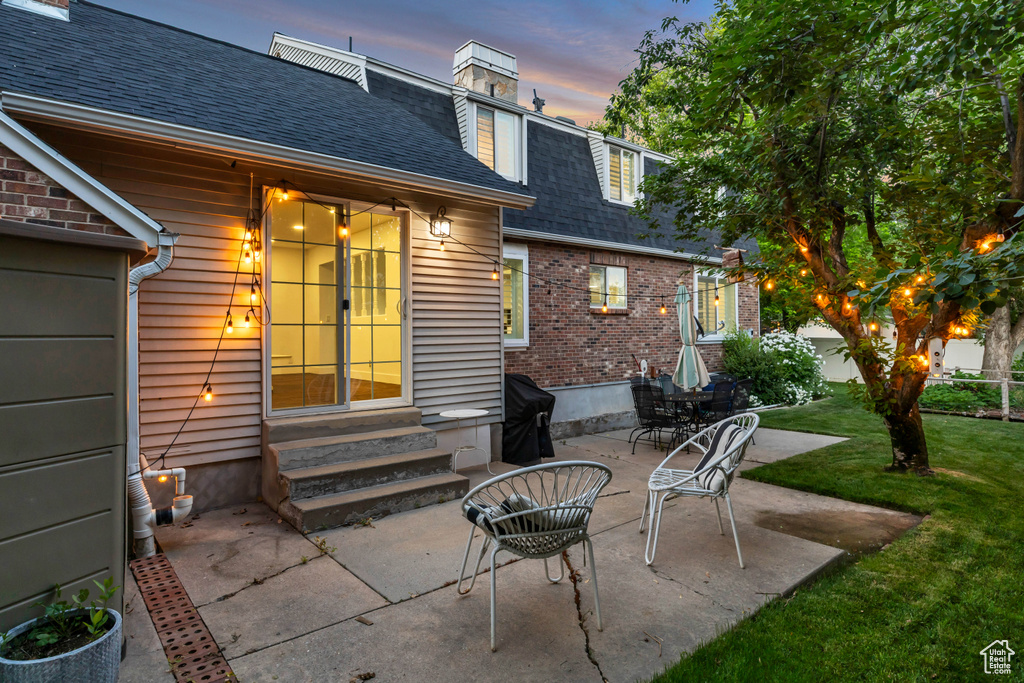 Patio terrace at dusk with entry steps, a patio, and a lawn