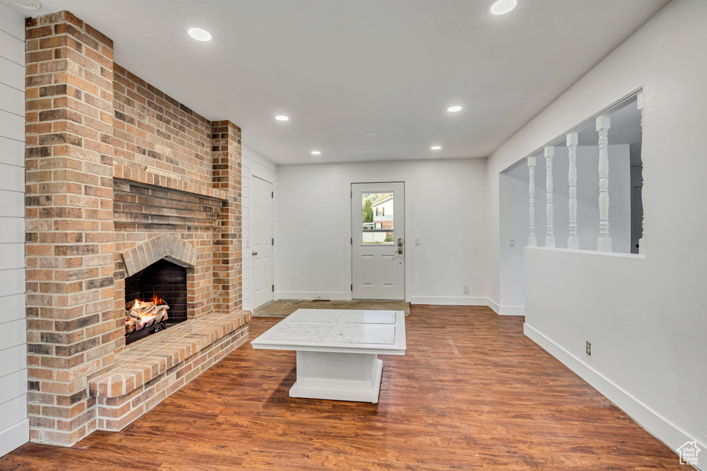 Unfurnished living room featuring recessed lighting, baseboards, a brick fireplace, and wood finished floors