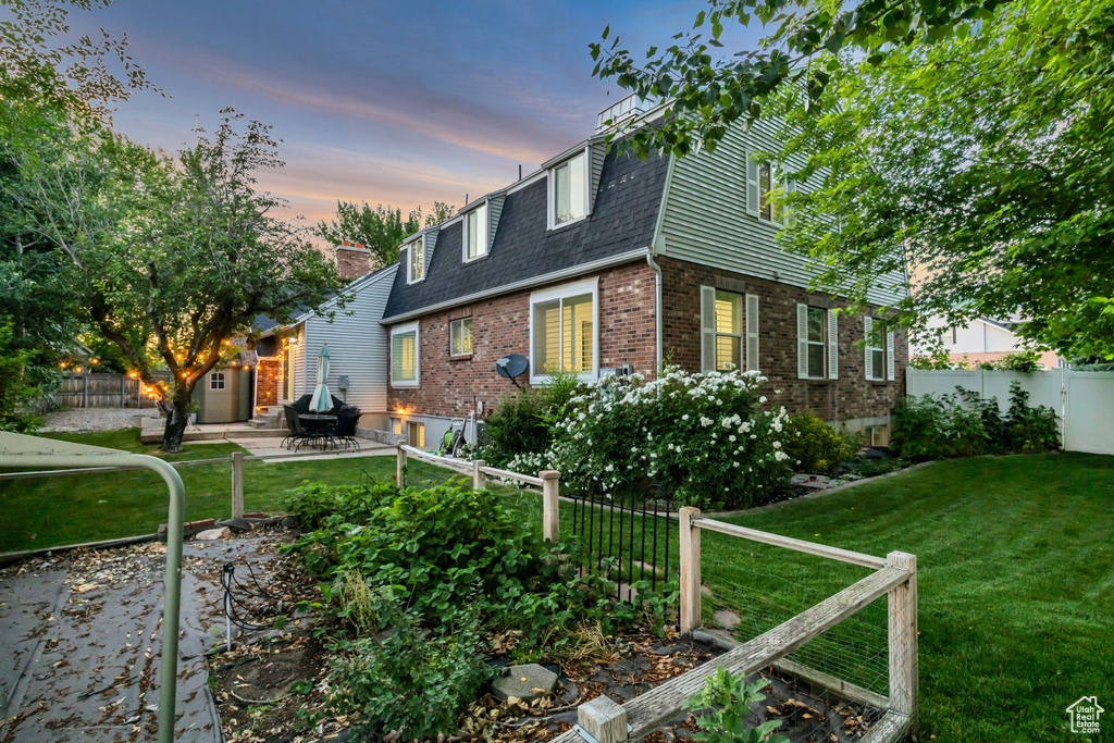 View of front of property with a shingled roof, brick siding, a patio, and mansard roof