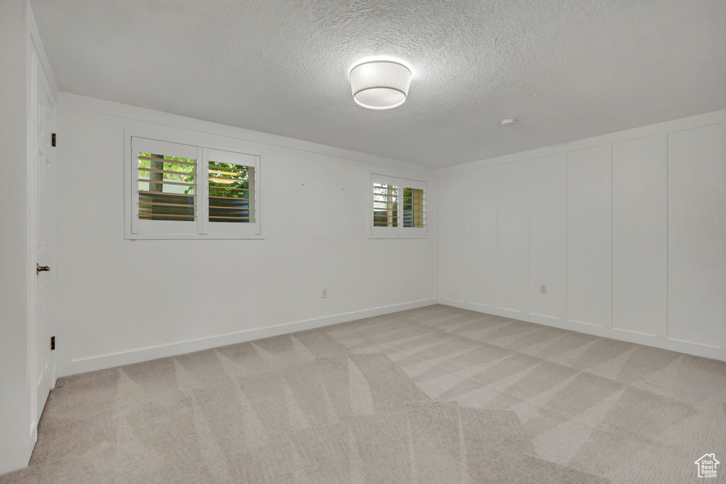 Unfurnished room featuring a textured ceiling, light carpet, and a decorative wall