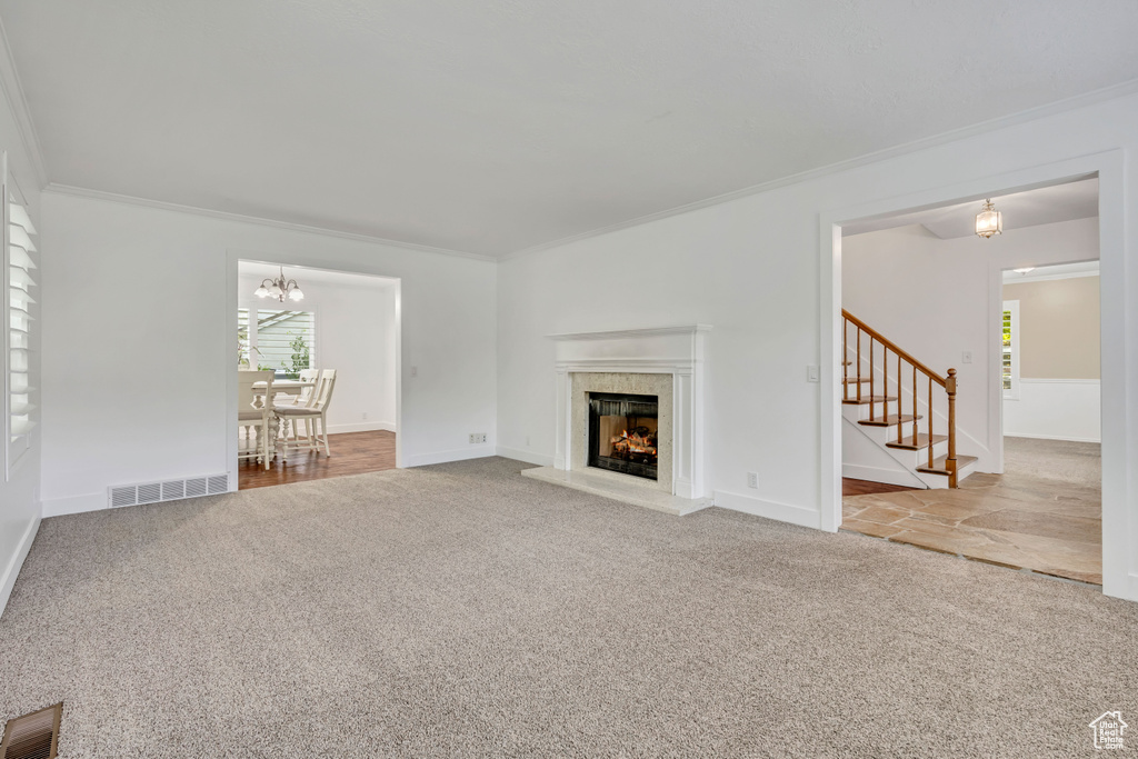 Unfurnished living room featuring carpet, crown molding, stairs, a chandelier, and a fireplace