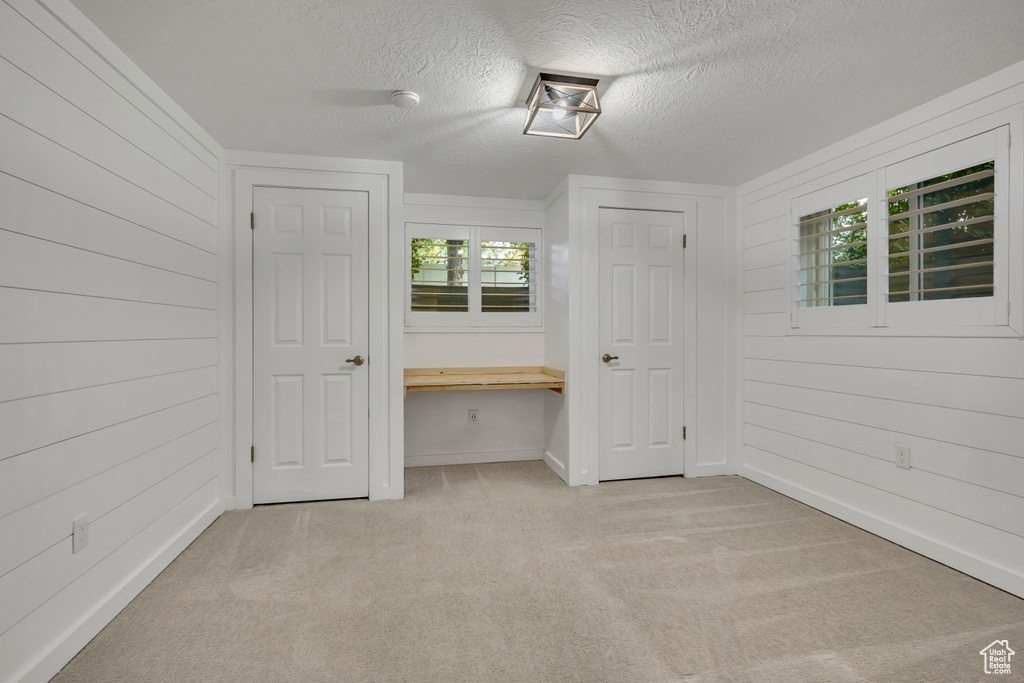 Unfurnished bedroom featuring light colored carpet, a textured ceiling, wood walls, and baseboards