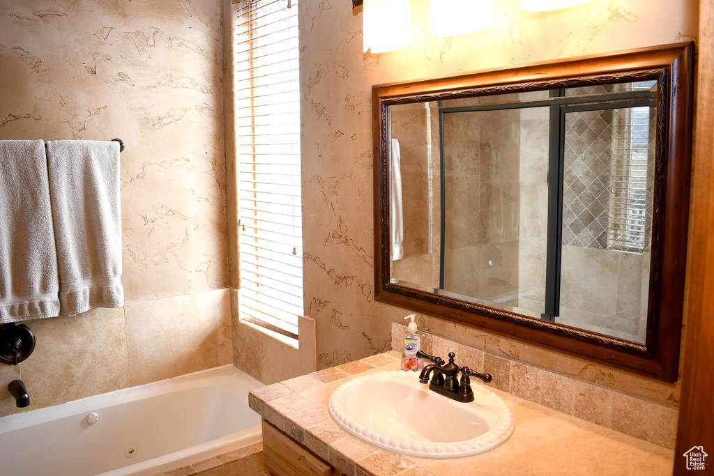 Bathroom with a tub with jets, vanity, and wallpapered walls