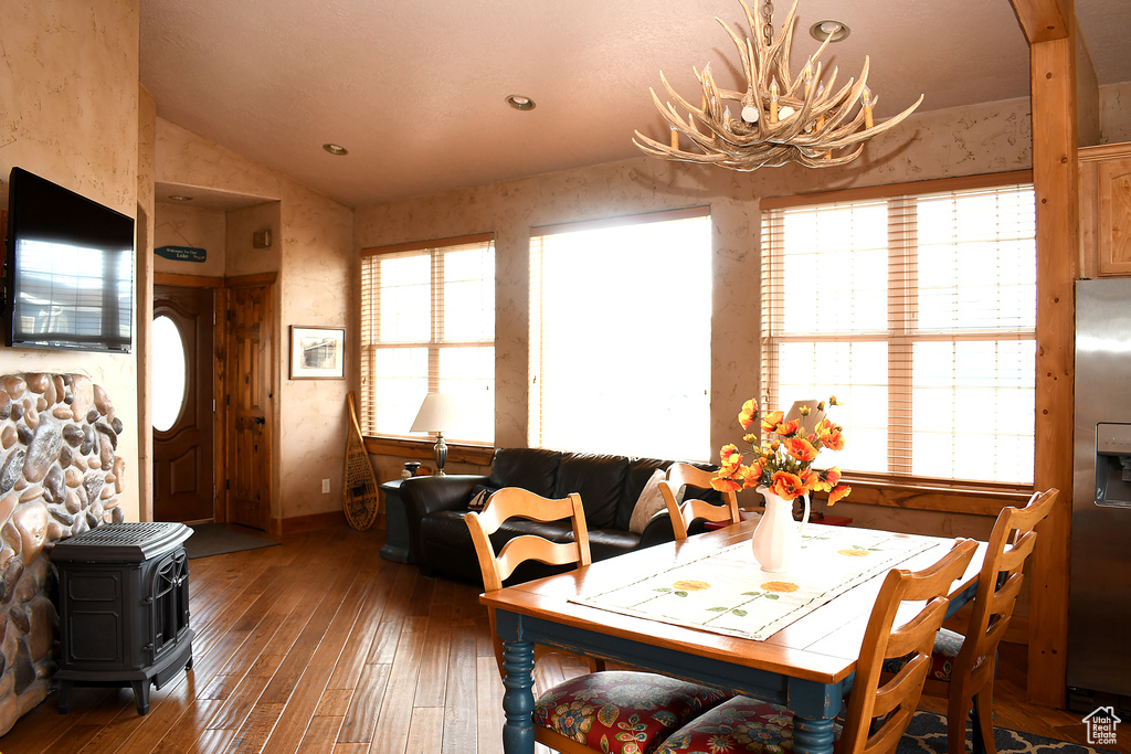 Dining space featuring vaulted ceiling, hardwood / wood-style flooring, a wood stove, baseboards, and a chandelier