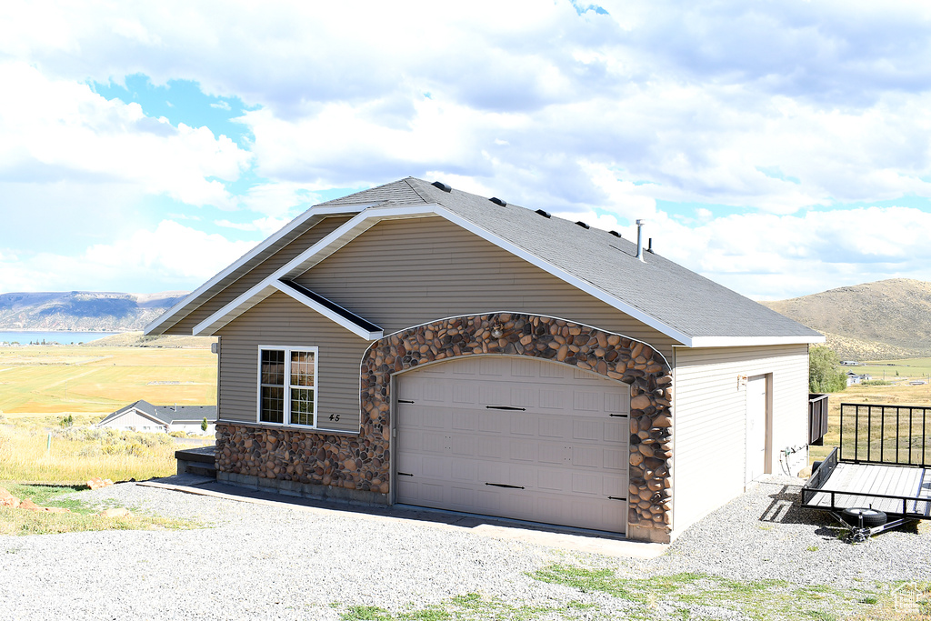 View of front facade featuring stone siding, a mountain view, a garage, and gravel driveway