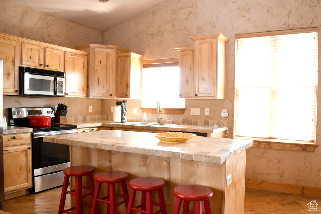 Kitchen with appliances with stainless steel finishes, light brown cabinetry, light wood-type flooring, a kitchen island, and wallpapered walls