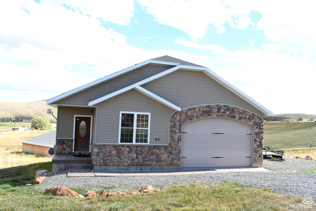 View of front of home with stone siding, an attached garage, and gravel driveway