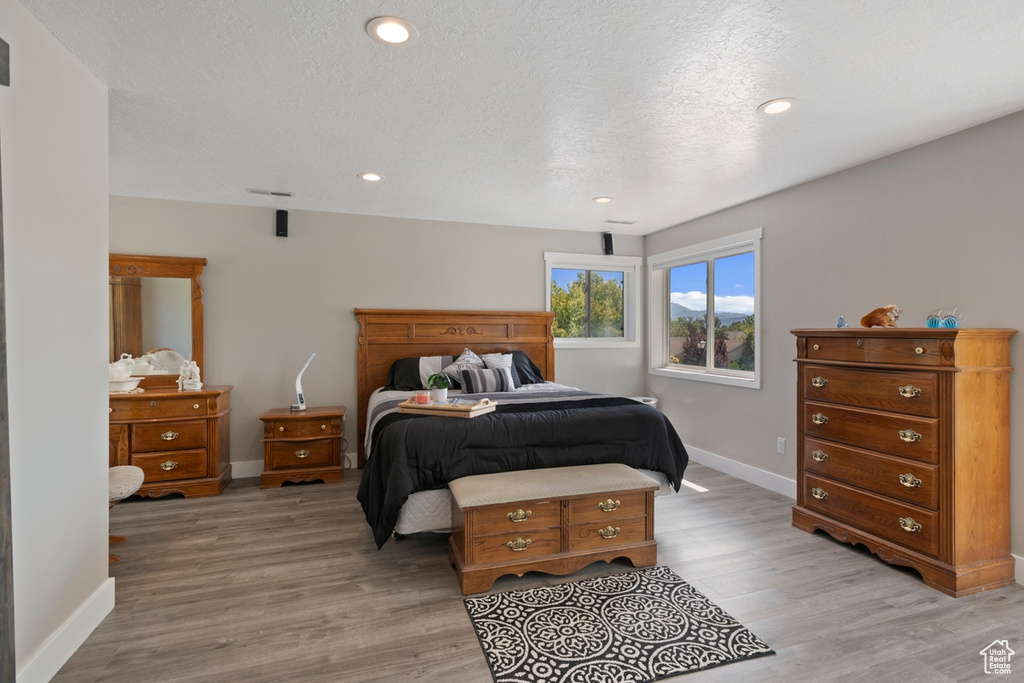 Bedroom featuring light wood-type flooring, baseboards, recessed lighting, and a textured ceiling