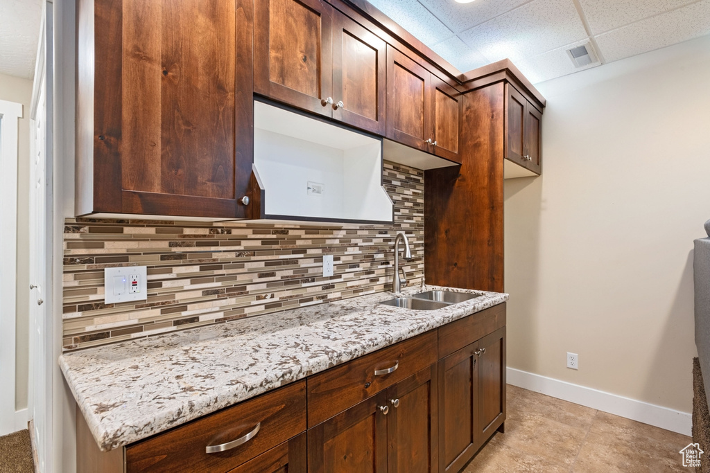 Kitchen with a sink, baseboards, decorative backsplash, a paneled ceiling, and light stone counters