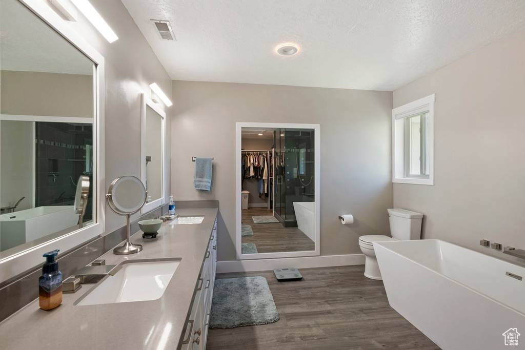 Full bath with toilet, wood finished floors, double vanity, a freestanding tub, and a stall shower