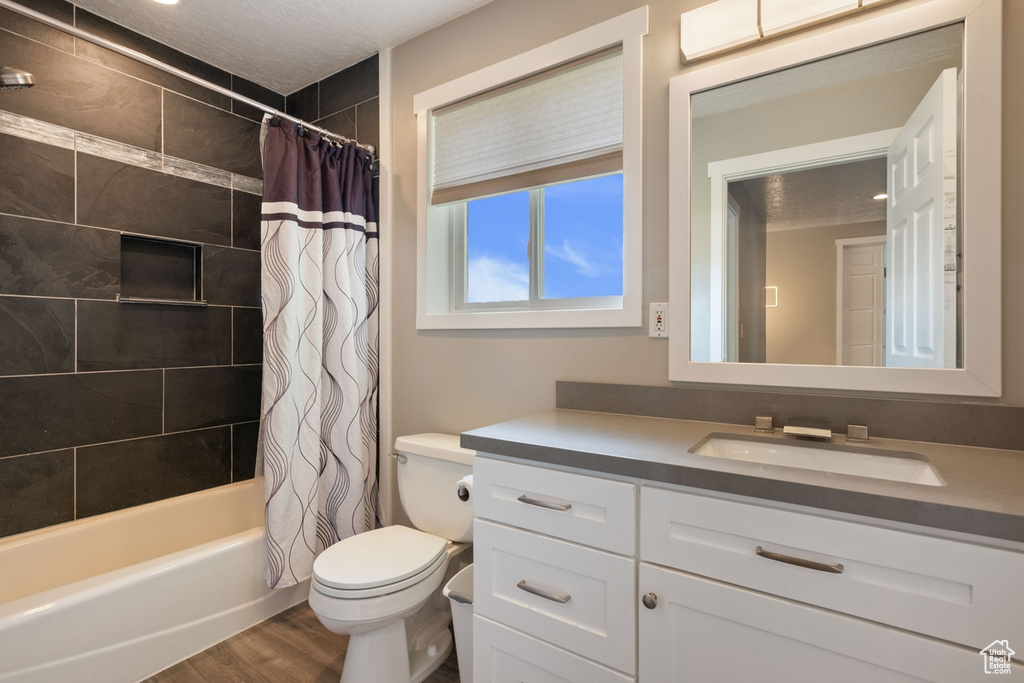 Bathroom featuring vanity, toilet, wood finished floors, shower / bath combination with curtain, and a textured ceiling