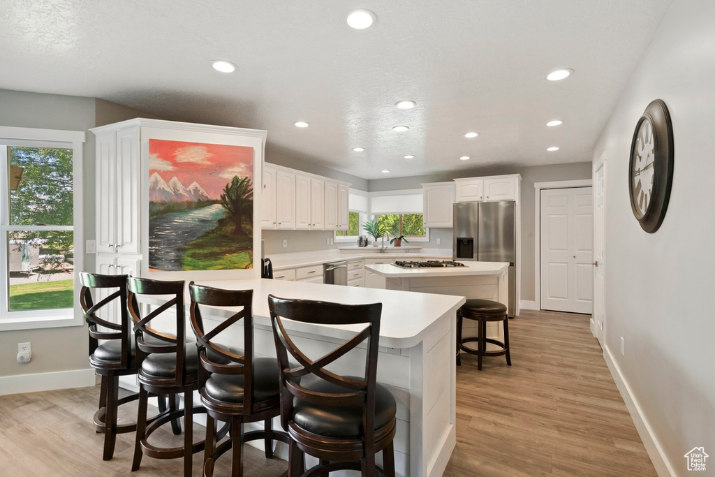 Kitchen featuring appliances with stainless steel finishes, recessed lighting, a kitchen bar, light wood-style floors, and baseboards