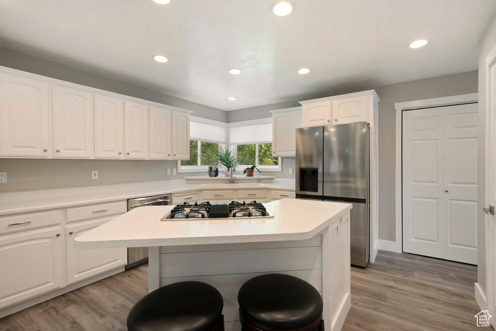 Kitchen with appliances with stainless steel finishes, a breakfast bar area, white cabinets, light wood-type flooring, and a center island