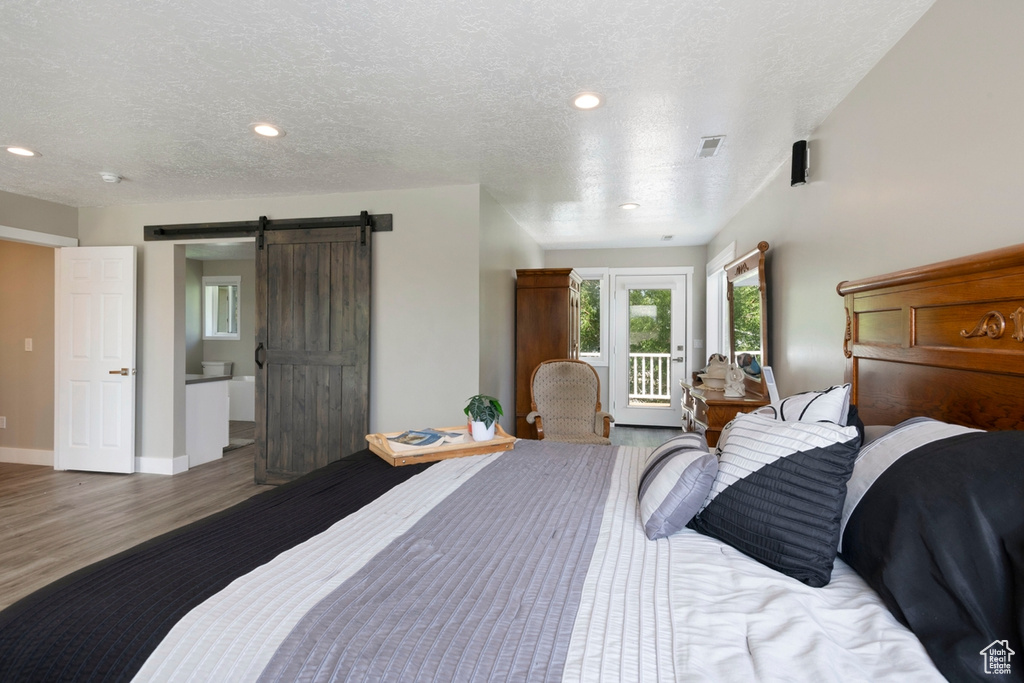 Bedroom featuring wood finished floors, a barn door, access to exterior, a textured ceiling, and recessed lighting