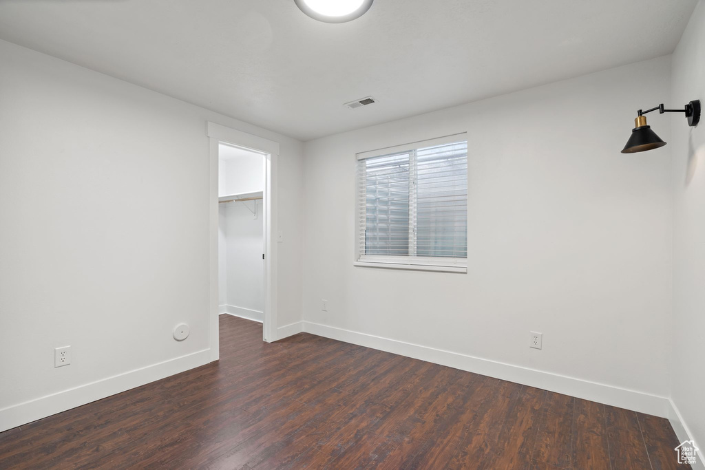 Unfurnished bedroom with baseboards, dark wood-style floors, a walk in closet, and a closet