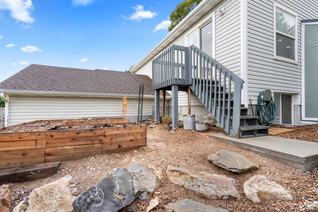 View of side of property featuring a garden, stairs, a shingled roof, and a deck