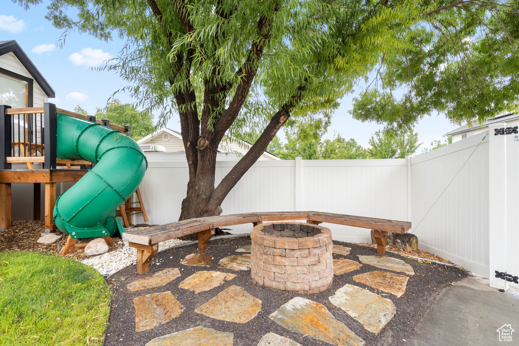 Fenced backyard featuring a fire pit, a playground, and a patio