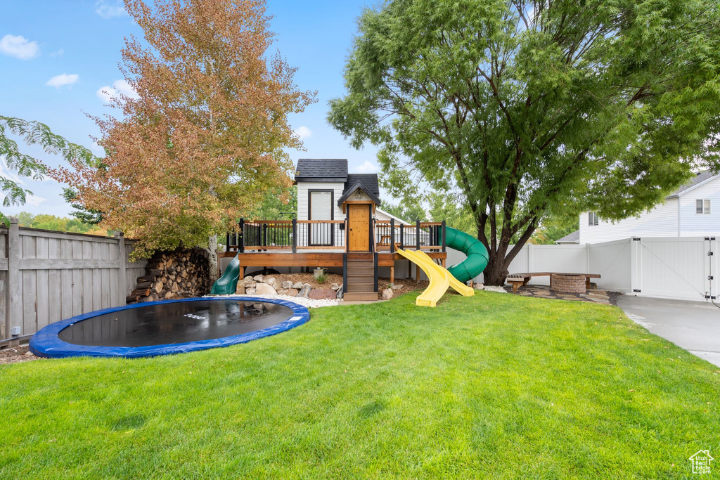 View of yard with a trampoline, a playground, and a gate