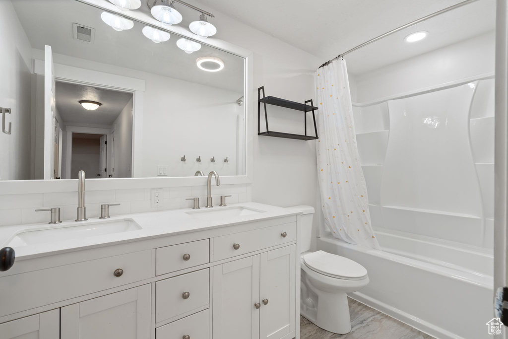 Bathroom featuring double vanity, shower / bath combo with shower curtain, and toilet