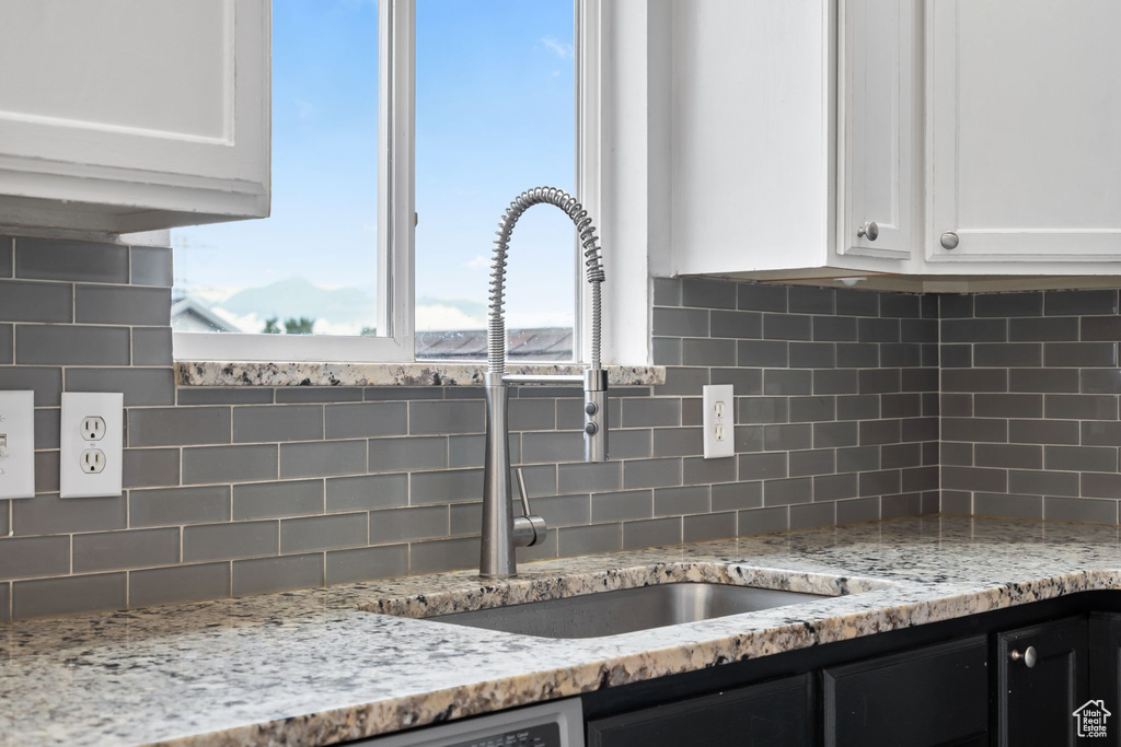 Kitchen view of a sink, white cabinetry, decorative backsplash, and light stone counters