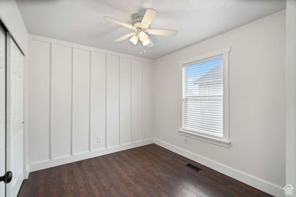 Empty room with dark wood-style flooring, baseboards, and a ceiling fan