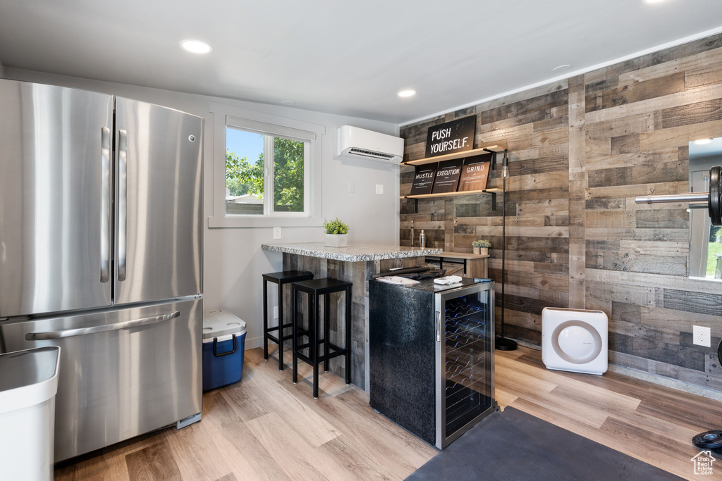Kitchen with freestanding refrigerator, a wall unit AC, wooden walls, beverage cooler, and a kitchen bar