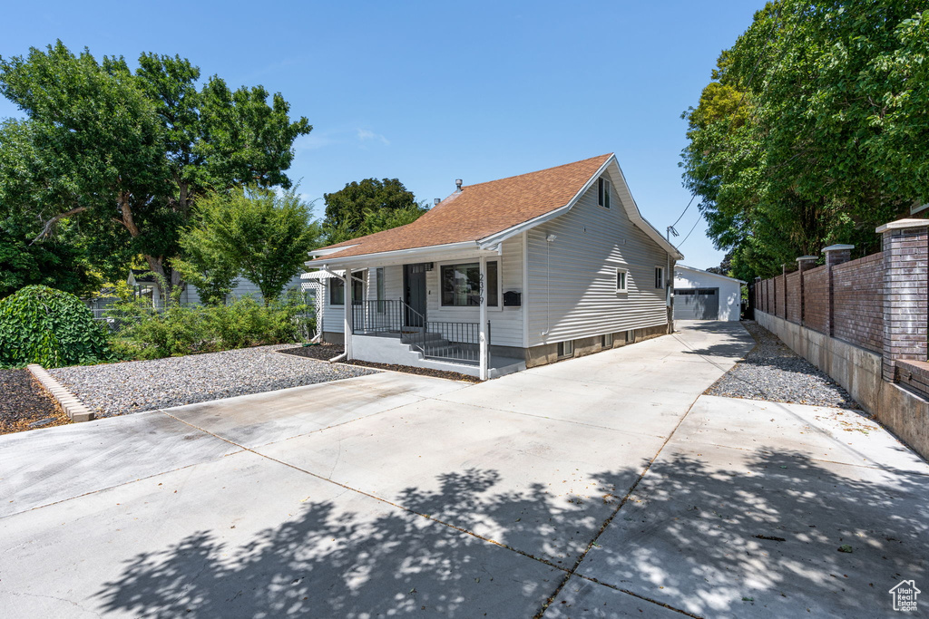 Rear view of property featuring a porch, an outbuilding, roof with shingles, and a garage