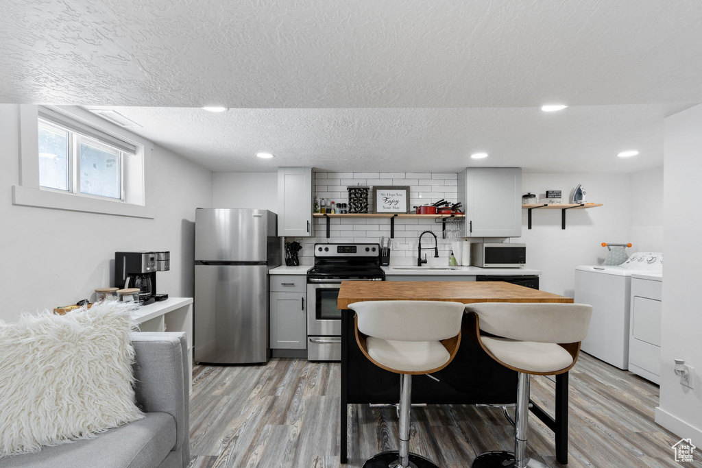 Kitchen featuring stainless steel appliances, open shelves, independent washer and dryer, a sink, and a textured ceiling