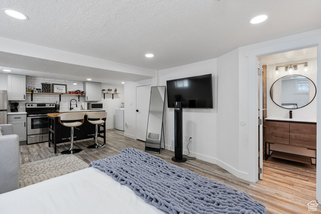 Bedroom featuring light wood-style floors, baseboards, recessed lighting, freestanding refrigerator, and a textured ceiling