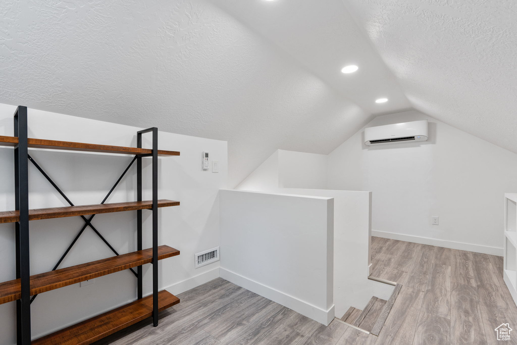 Bonus room featuring an AC wall unit, a textured ceiling, vaulted ceiling, wood finished floors, and baseboards