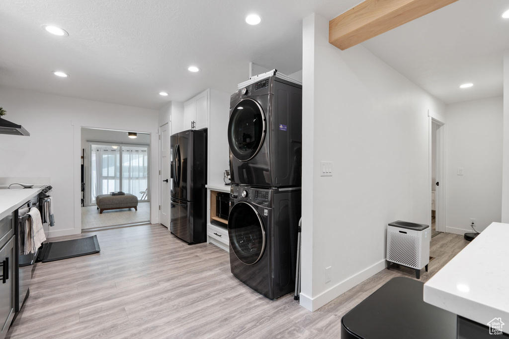Kitchen featuring stacked washer / drying machine, black fridge, light countertops, light wood-style flooring, and recessed lighting