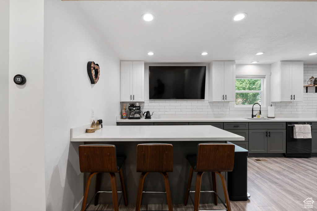 Kitchen featuring black dishwasher, a kitchen breakfast bar, tasteful backsplash, white cabinetry, and recessed lighting