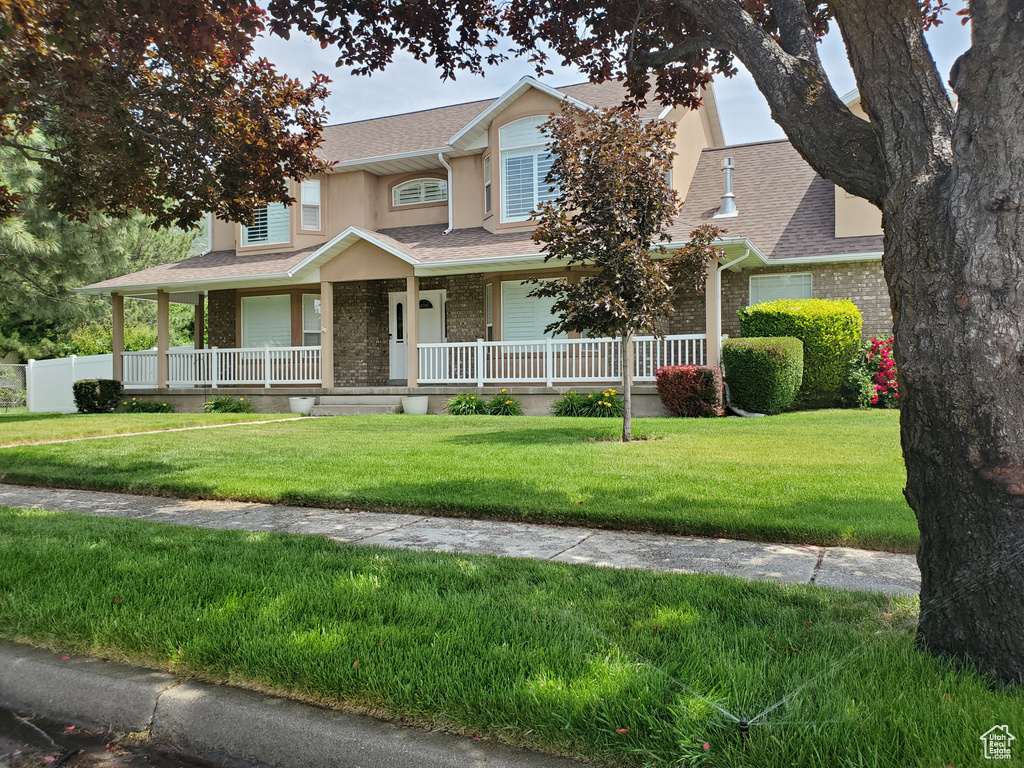 View of front of house featuring brick siding, covered porch, a shingled roof, a front lawn, and stucco siding