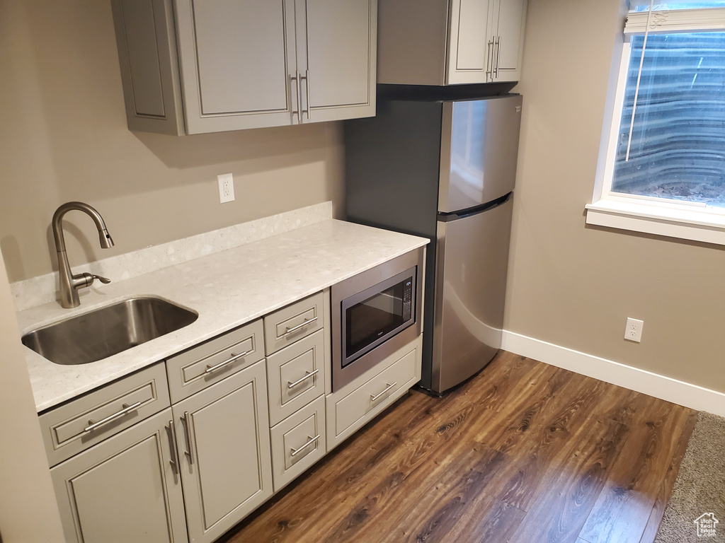 Kitchen with appliances with stainless steel finishes, a sink, gray cabinetry, dark wood finished floors, and light countertops