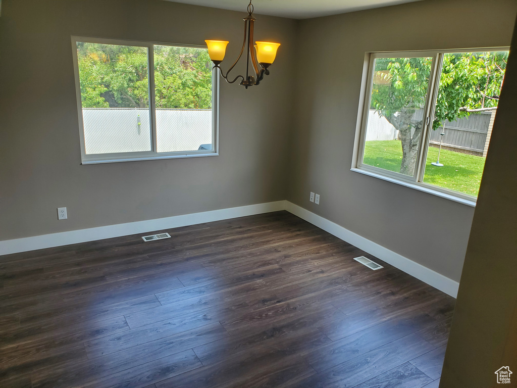 Empty room with a chandelier, dark wood finished floors, and baseboards
