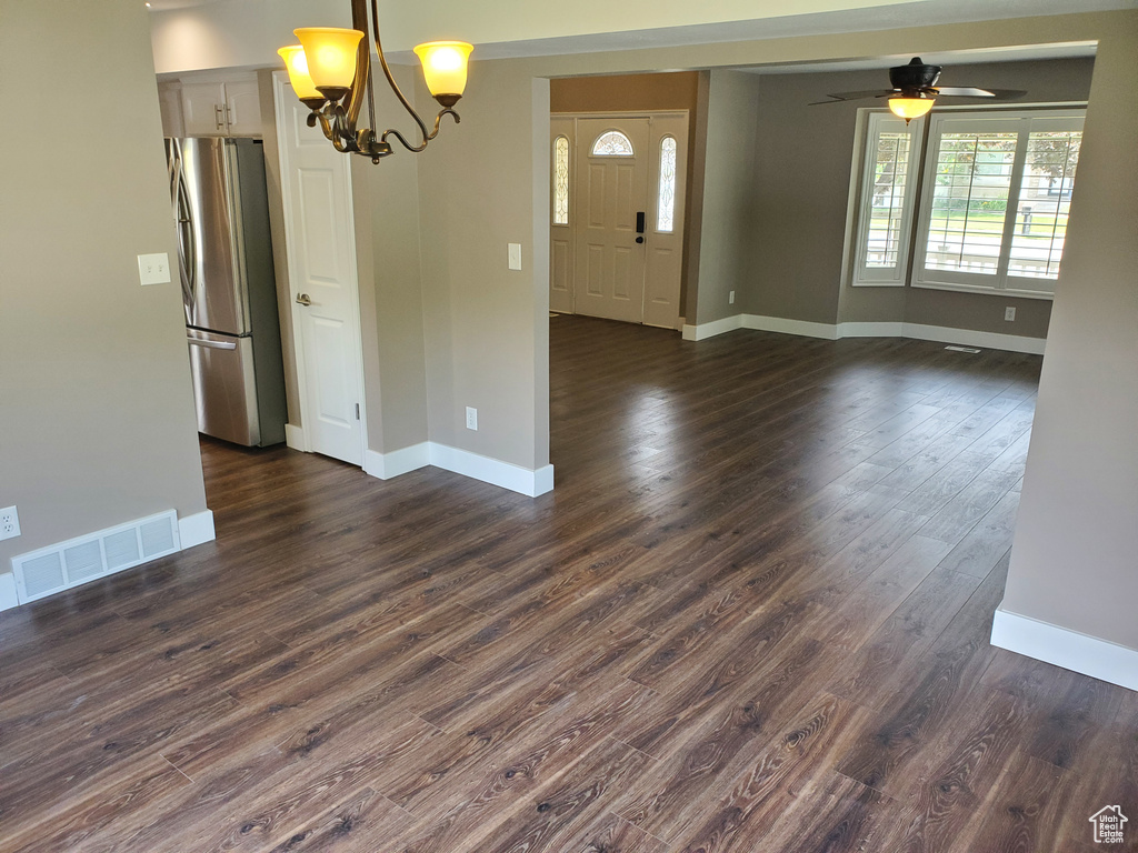 Empty room featuring a ceiling fan, a chandelier, baseboards, and dark wood-type flooring
