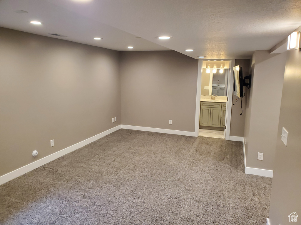 Finished below grade area with light carpet, baseboards, recessed lighting, and a sink