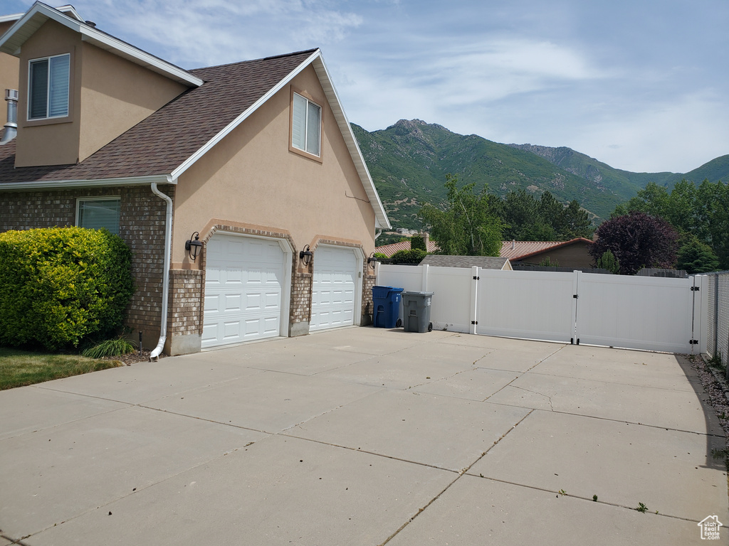 View of home's exterior with a gate, stucco siding, a mountain view, and roof with shingles