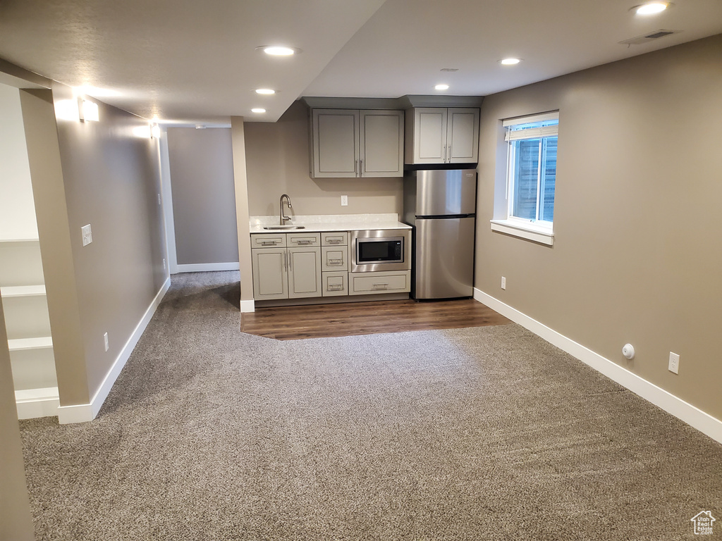 Kitchen with appliances with stainless steel finishes, dark carpet, baseboards, gray cabinetry, and recessed lighting