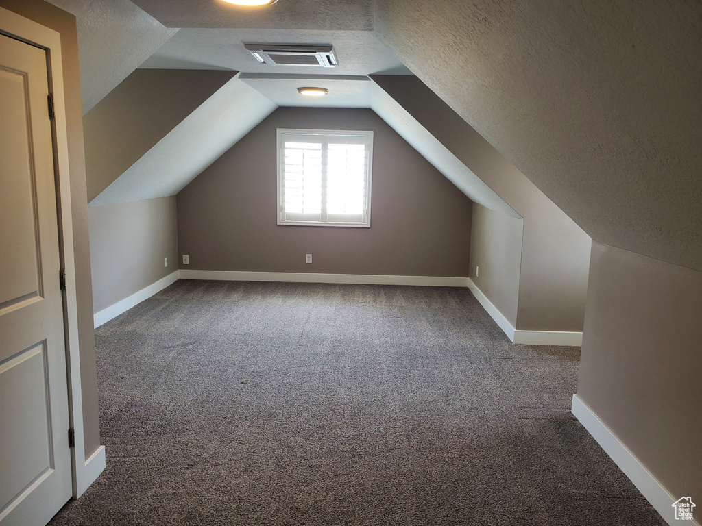 Bonus room with carpet, a textured ceiling, lofted ceiling, and baseboards