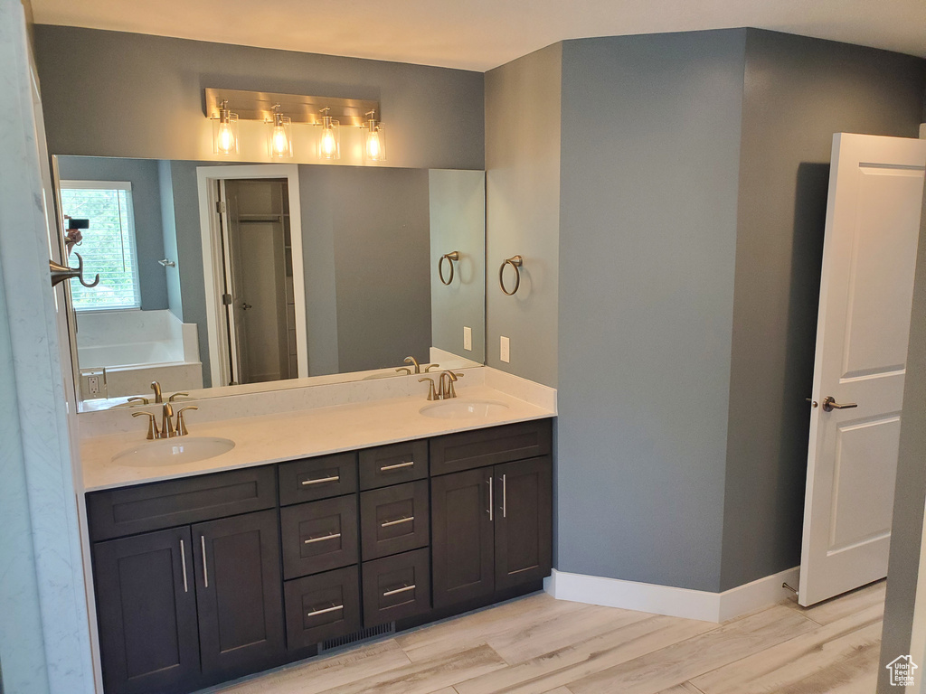 Full bathroom featuring double vanity, wood finished floors, a garden tub, and baseboards